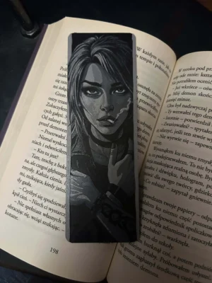 Zakładka 3D z portretem kobiety w czerni i szarościach, umieszczona w książce