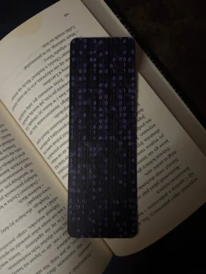 Zakładka 3D z fioletowym wzorem kodu binarnego 0/1, leżąca na otwartej książce