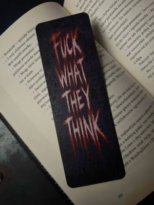 Zakładka 3D z czerwonym napisem "F*CK WHAT THEY THINK" leży na otwartej książce